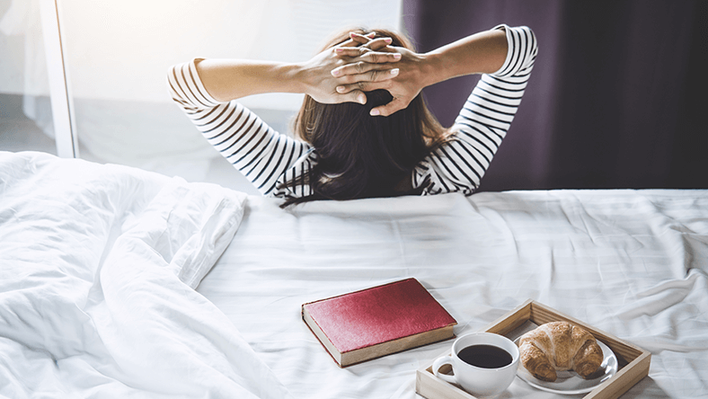 Woman relaxing against bed at home on a staycation holiday