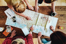 Four friends standing around a map of the world plotting their next holiday destination