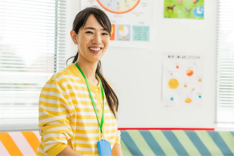 A woman wearing a yellow and white striped shirt stands in a brightly lit classroom.