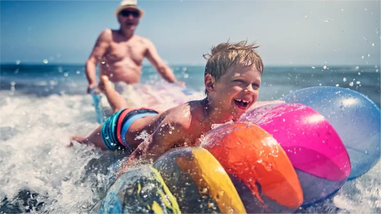 A child and their relative have fun playing in the ocean at the beach.