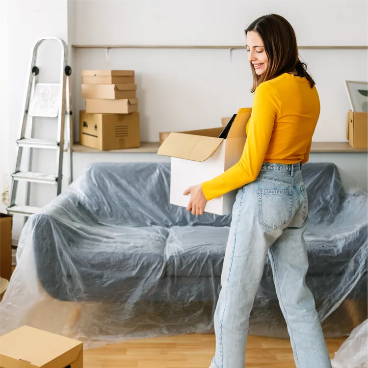 A young woman carries a cardboard box in her new living room.