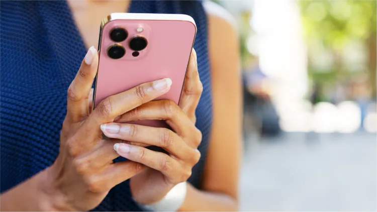 A woman holds a pink smartphone not showing the screen just the back, while outdoors