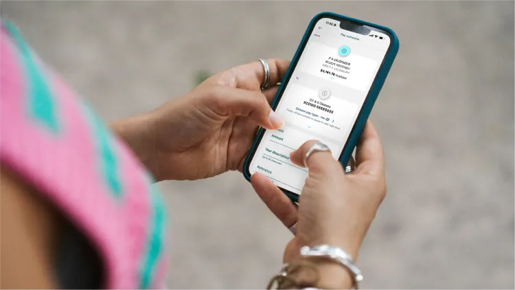 A person holds a smartphone displaying a financial transaction screen with the text 'TRANSFER MONEY'.